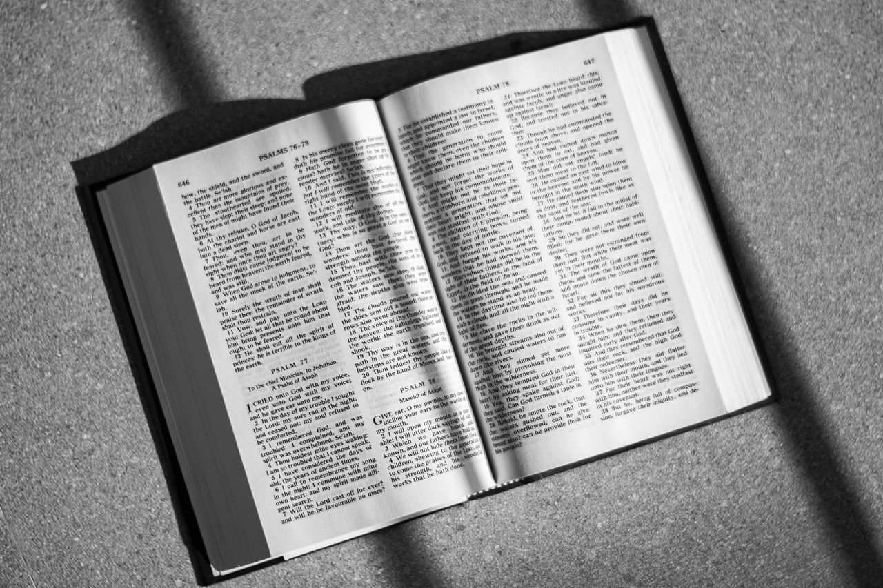 A black and white photo of an open Bible on the floor, featuring shadows.