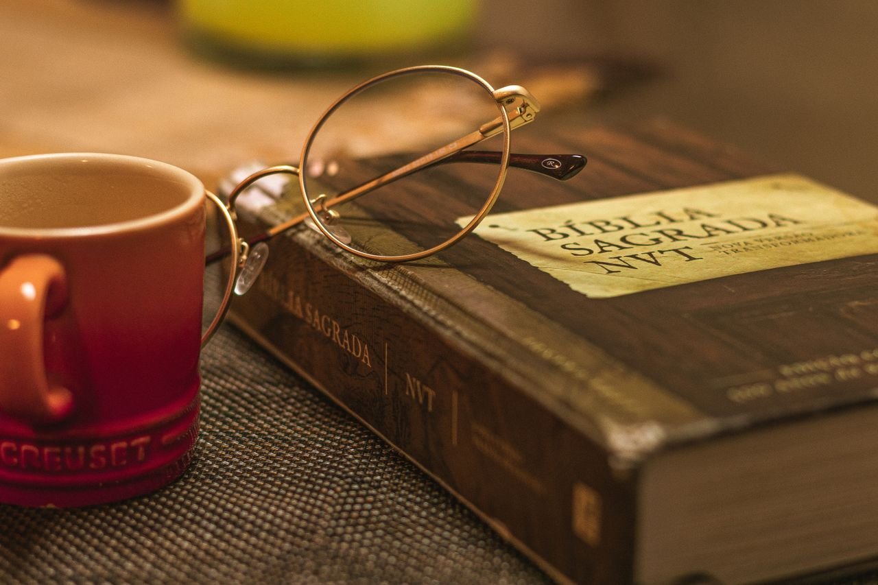 A Biblia Sagrada with glasses rests on a table beside a red mug, symbolizing relaxation and reflection.