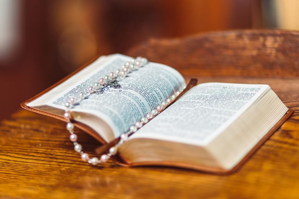 An open Bible with a detailed rosary lying on its pages resting on a wooden surface.
